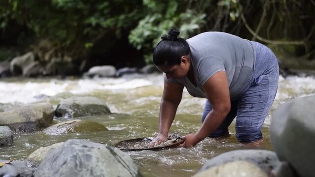 Latin American woman searching river sediment by hand for artisanal gold, artisanal mining
