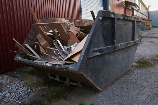 Construction waste container filled with discarded wood and cardboard materials. Large industrial skip bin at a commercial site, demolition debris, waste management, recycling and material disposal