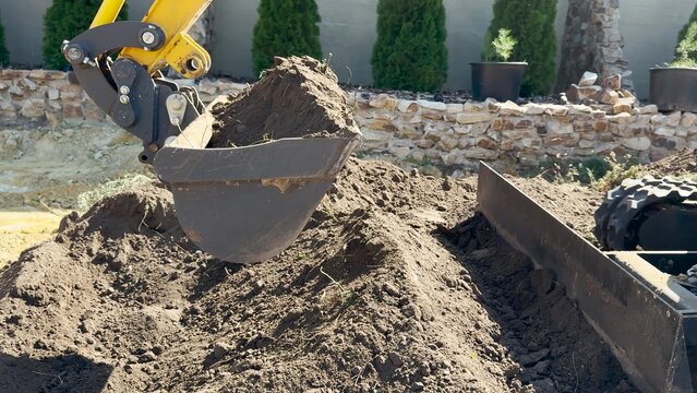 Bucket tracked excavator levels the ground in backyard house. Mini excavator scoops up soil, construction work supervised engineer. Earthworks being carried out using excavator. Building, Earthmoving