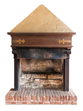 Antique medieval-style indoor fireplace featuring a weathered brick hearth, dark wooden lintel decorated with ornate brass hinges, and a textured plaster pyramidal chimney hood, isolated