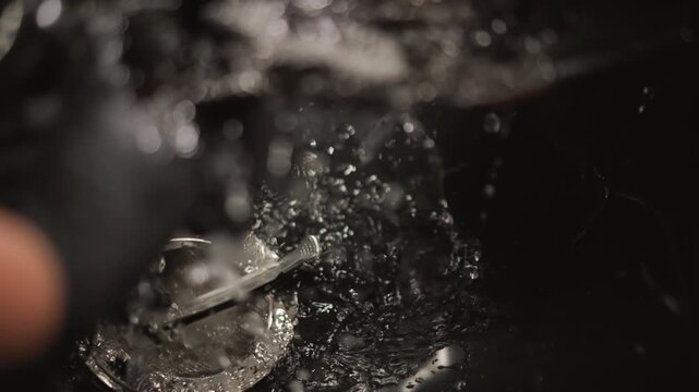 Close up view of metal comb submerged in soapy water. Gloved hand moves indicating tool handling or placement into sink for further submersion hair tools