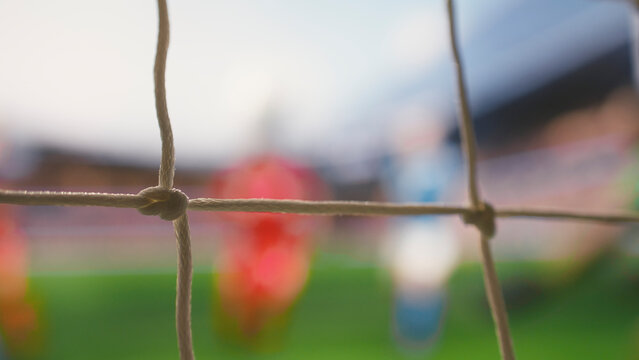 Selective focus of soccer ball crossing line of goal frame on pitch, goal shot hitting net, red soccer players of winning team cheering near defeated opponents, fallen goalie in blurred motion.