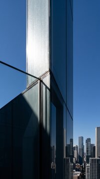 Minimal glass tower corner reflecting downtown financial district office skyline in sharp light