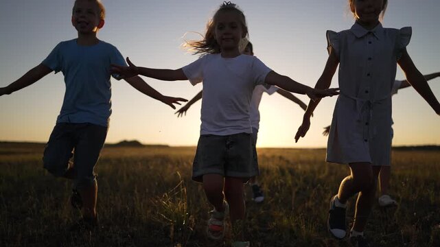 Happy children run with arms outstretched toward camera at sunset. Smiling kids play freely across grass field. Group of running children laugh in summer meadow. Kids enjoy golden hour outdoors.