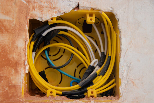 Yellow recessed junction box in wall with organized coiled wiring. Focus on electrical installations, renovation, construction, and building infrastructure.