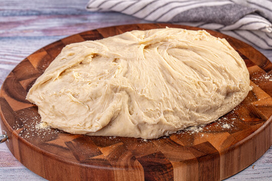 Fresh bread dough resting on round wooden cutting board with flour dusting, artisanal baking preparation
