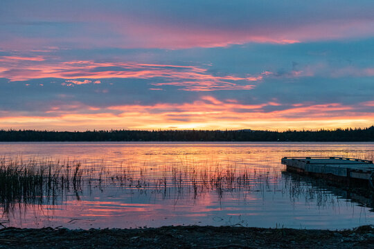 Colorful sunrise over reflective lake with fishing dock