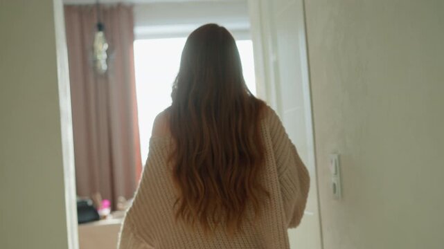 Young lady moves through interior space her back to camera as woman progresses into brighter areas. setting is softly lit with neutral tones suggesting calm domestic or transitional moments