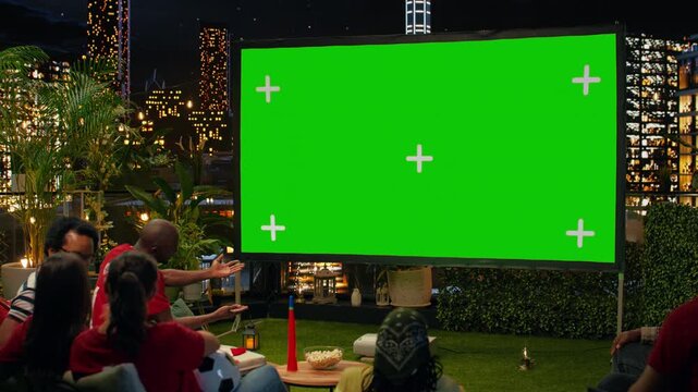 Football supporters use an isolated projection screen on an outdoor rooftop to watch the game, with a chroma key display for group sports entertainment.