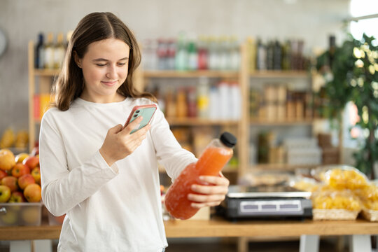 Teen girl in store scans QR code on grapefruit juice bottle. With help of mobile appl, buyer receives information about product. She checks manufacturers data in registry database of national agency