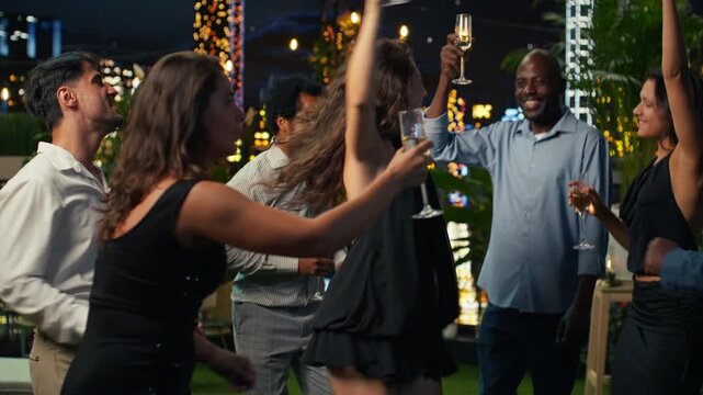 Ecstatic woman dances among partygoers during a celebration as delighted friends enjoy music and champagne together in a stylish terrace lounge.