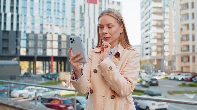 Upset unhappy Caucasian businesswoman girl using smartphone bad connection losing fortune loss fail touch head why negative result outdoors. Mature traveler in coat standing on downtown city street.