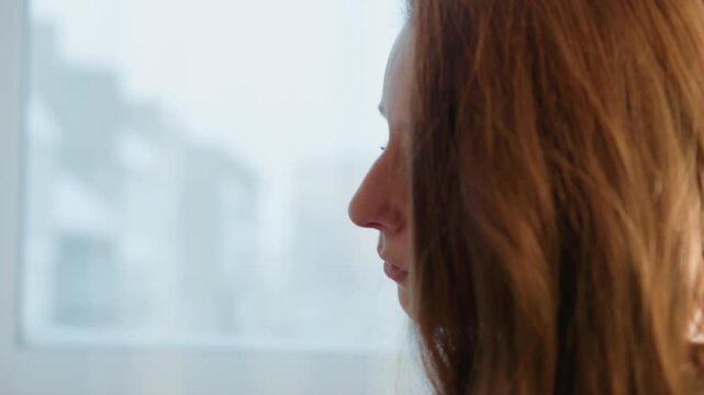 Close up side view shows right half of woman face and shoulder. subject has medium to long brown hair with soft lighting creating gentle highlights. Background is blurred suggesting indoor