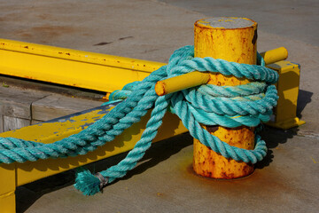 Turquoise mooring rope tied around yellow harbor bollard © Comofoto