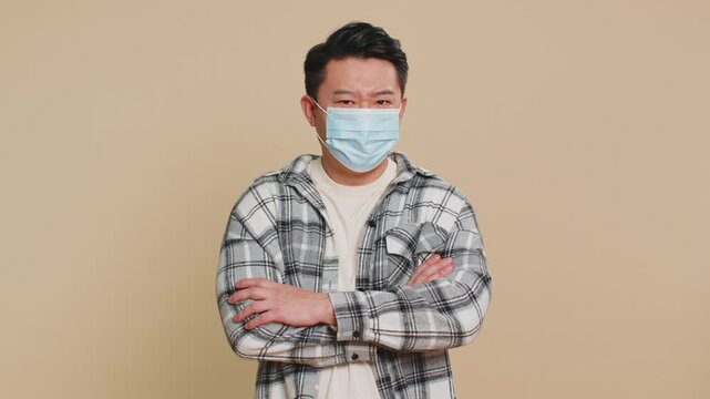 Asian middle-aged ill man wearing medical mask on face prevention protection safety bronchitis asthma allergy flu pneumonia virus disease problem. Sick mature Chinese guy isolated on beige background