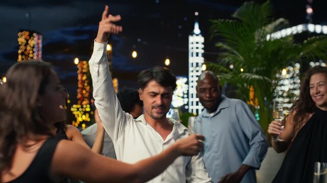 Thrilled man cheers and dances at an anniversary party, energizing nearby partygoers with confident dance moves in a lively outdoor setting.