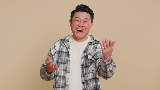 Asian middle-aged man pointing finger to camera, laughing out loud, taunting making fun of ridiculous appearance, funny joke anecdote, bullying, abuse. Adult Chinese guy isolated on beige background