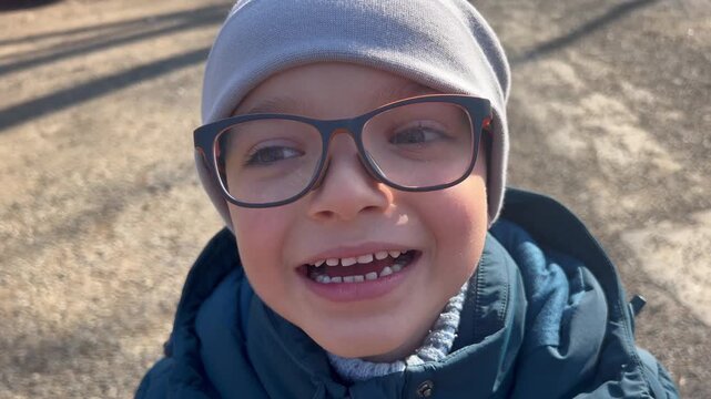 seven year old boy with glasses smiling and showing changing baby teeth in close up outdoors, concept of tooth development, pediatric dentistry, growing childhood