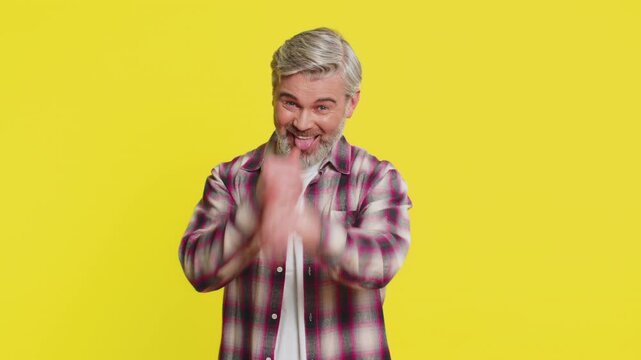Caucasian, middle-aged mature man on yellow background showing carefree fun with tongue out and silly face. Lighthearted mischief, playful mood, highlighting comedic energy and easygoing attitude