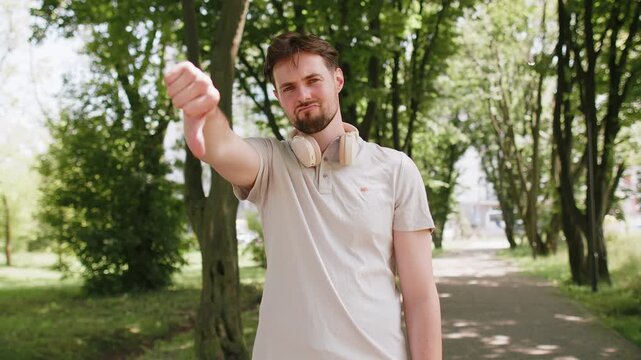 Sad upset dissatisfied loser man jogger shows thumb down bad result unmotivated disagree dislike standing on footpath in park, sport failure fitness guy hard ineffective exercise workout athlete fail