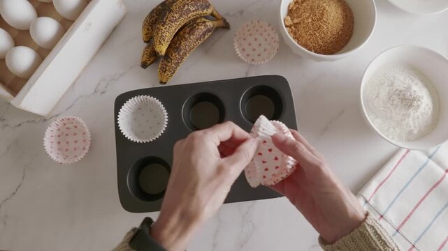 Woman hands putting cupcake liners on a cupcake pan and ingredients for baking banana muffins.