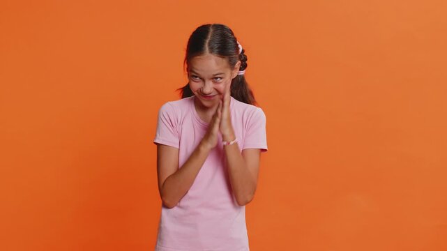 Sneaky cunning preteen child girl kid with tricky face gesticulating and scheming evil plan, thinking over devious villain idea, cheats, jokes, pranks. Teenager children isolated on orange background
