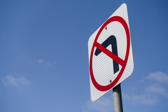 a Australian "No Left Turn" road traffic sign against blue sky, featuring a red prohibition circle and slash over a black left-pointing arrow on a reflective white square board. Victoria, Australia