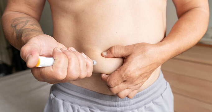 Man gives himself subcutaneous injection of insulin with an auto-injector into abdominal area, capturing fold of skin. Concept of obesity therapy and weight loss with injectable drugs