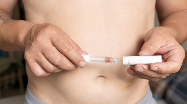Hands of mature man hold syringe pen, ready for subcutaneous injection into abdomen. Therapy for obesity and weight loss using injectable drugs. Controlling diabetes, metabolism at home