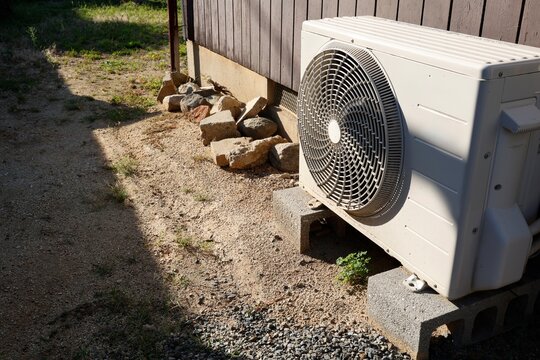 日光に照らされたエアコンの室外機。木製外壁脇の屋外設備