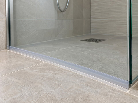 Clear shower threshold strip along tiled floor beside a glass enclosure