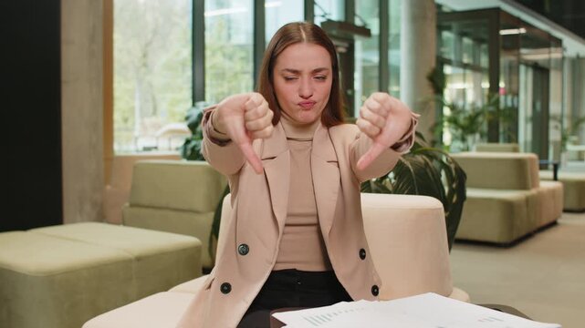 Dislike. Upset Caucasian business woman sitting in office lobby showing thumb down sign gesture, expressing discontent, disapproval dissatisfied bad work. Displeased serious freelancer girl in formals