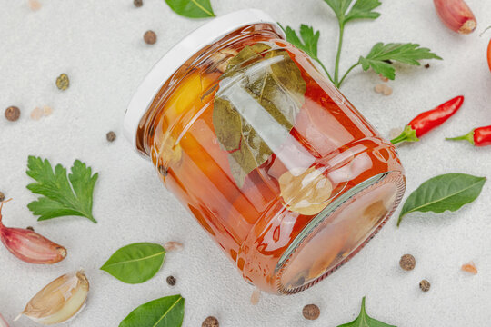 Glass jar of fermented probiotic tomatoes with garlic, herbs, and spices on light background