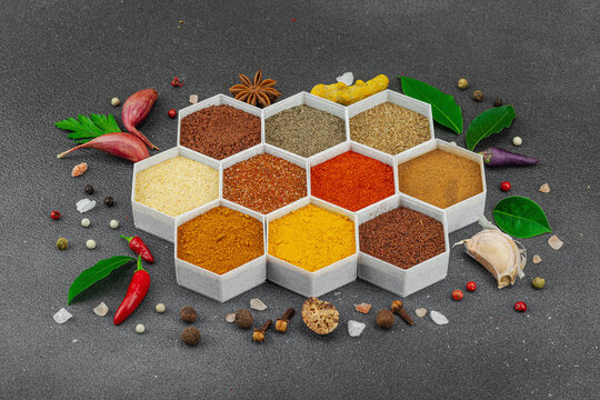 Spices set in hexagonal containers with fresh herbs, garlic, tomatoes, and chili peppers on dark
