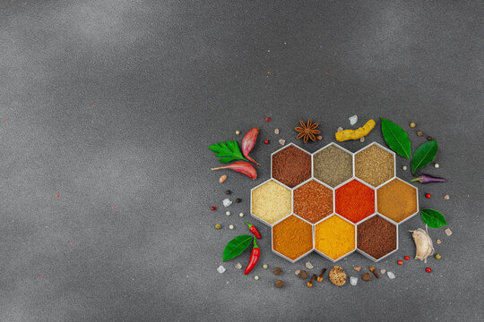 Spices set in hexagonal containers with fresh herbs, garlic, tomatoes, and chili peppers on dark