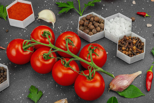 Culinary background with vine tomatoes, garlic, spices, salt, and herbs scattered on a dark surface