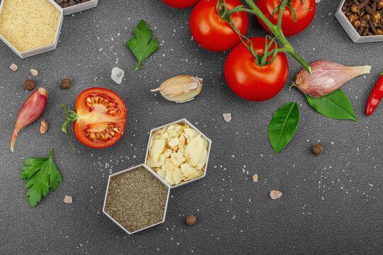 Culinary background with vine tomatoes, garlic, spices, salt, and herbs scattered on a dark surface