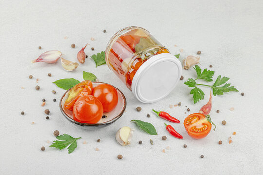 Glass jar of fermented probiotic tomatoes with garlic, herbs, and spices on light background