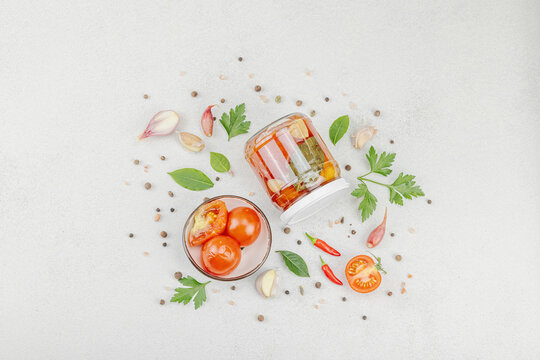 Glass jar of fermented probiotic tomatoes with garlic, herbs, and spices on light background