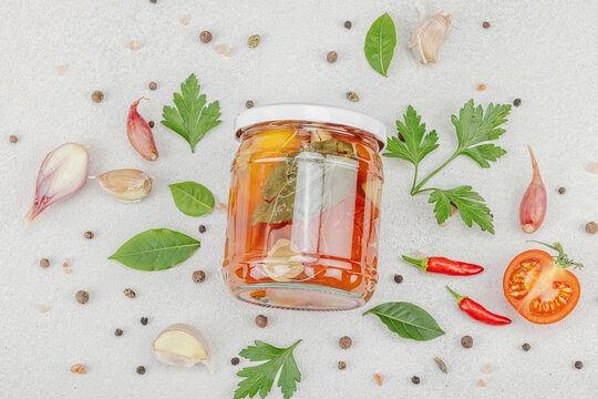 Glass jar of fermented probiotic tomatoes with garlic, herbs, and spices on light background