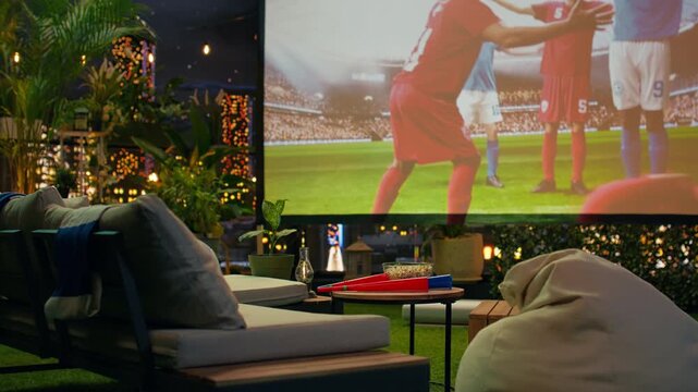 Football game viewing setup on rooftop terrace with seating and fan props arranged around projected match, creating casual watch party atmosphere for relaxed sports viewing above city.