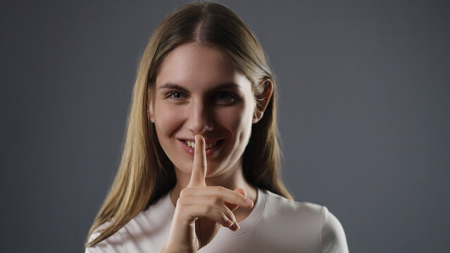 Young woman smiling, keeping secret by shushing with finger on lips
