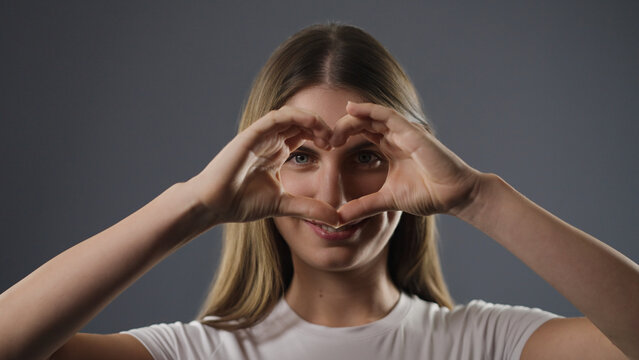 Young woman looking through a heart shape formed with her hands, smiling at the camera