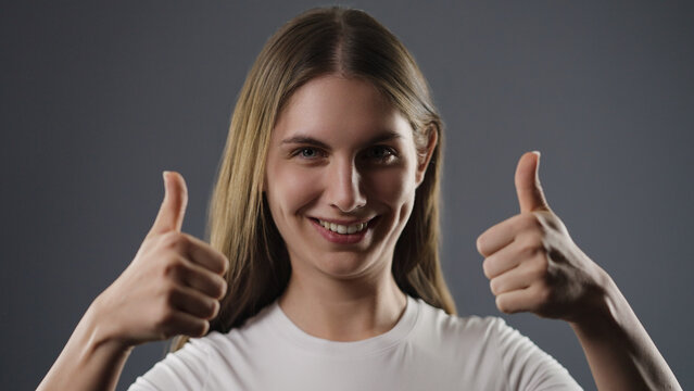 Young woman smiling while giving two thumbs up, showing approval and success