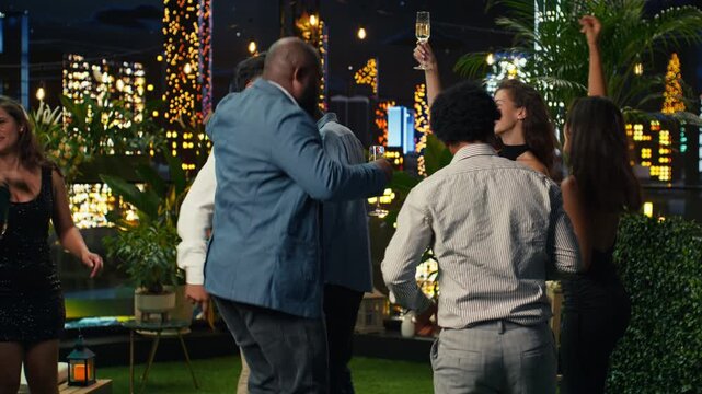 Cheerful friends dance on a rooftop terrace at night as energetic partygoers enjoy music and the nightlife atmosphere above the city lights.