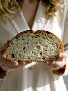 A person holds a large, halved loaf of artisanal bread, showcasing its airy crumb structure.