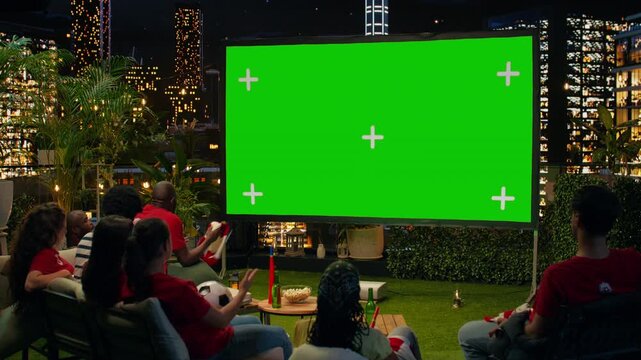 Seated soccer supporters watch a match on a rooftop terrace using a mockup projection screen, with chroma key display space for live sports streaming.