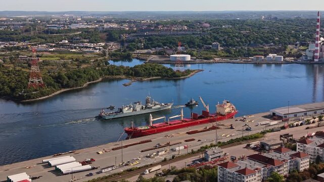 High-angle aerial view of a military vessel towing another ship through Halifax Harbour, passing under a bridge in Halifax, Nova Scotia, during the early morning hours.