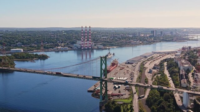 Cinematic drone footage of a military ship towing a vessel across Halifax Harbour at dawn, moving beneath a bridge in Nova Scotia, Canada, with peaceful morning waters surrounding the ships.