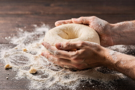 Baker Shaping Bagel Dough with Flour on Wooden Table